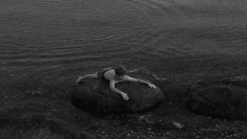 a man is laying on a rock in the water .
