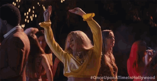 a woman in a yellow top is dancing at a party with #onceuponatimeinhollywood written on the bottom