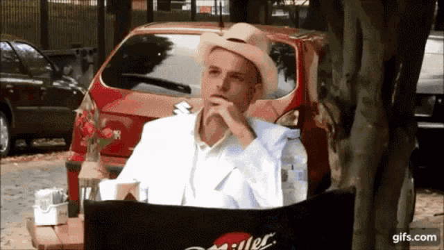 a man wearing a hat sits in front of a red miller lite car