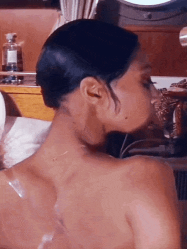 a woman without a shirt is taking a bath and looking at her back .