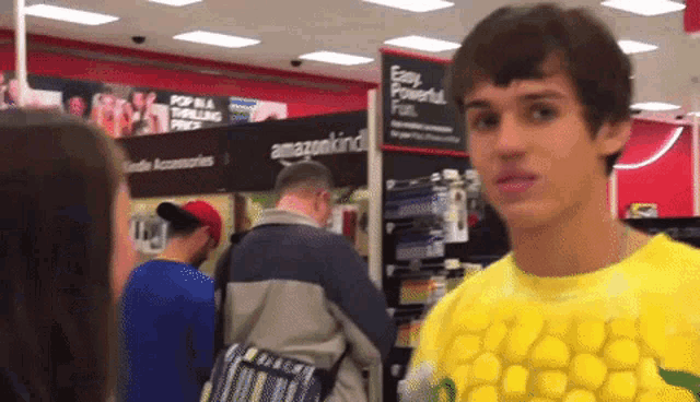 a man wearing a yellow corn on the cob shirt stands in front of a sign that says easy powerful fun
