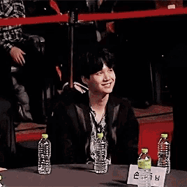 a man is sitting at a table with bottles of water and a sign on it .