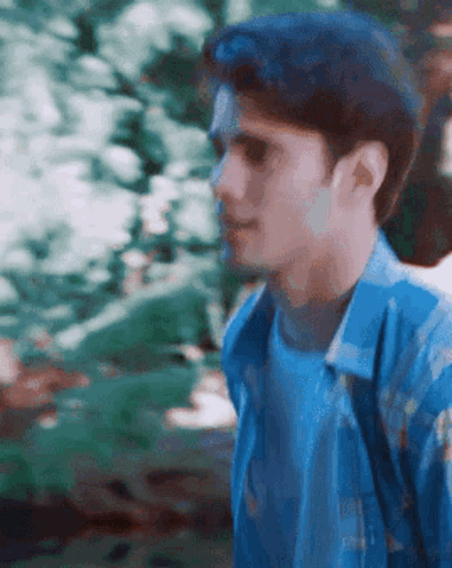 a man in a blue shirt is talking to another man in the woods .