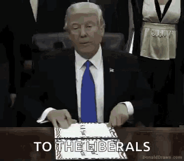 a man in a suit and tie is sitting at a table with a cake and a sign that says to the liberals