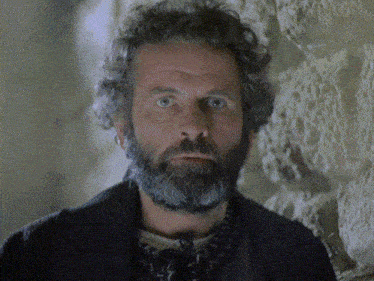 a man with a beard and curly hair is looking at the camera