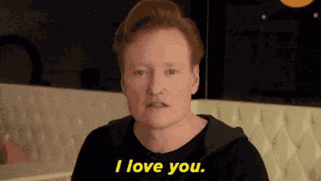 a man with red hair says i love you in front of a white couch