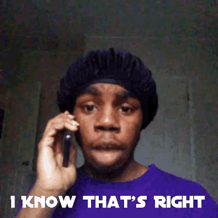a man in a purple shirt is talking on a cell phone while wearing a black hat .