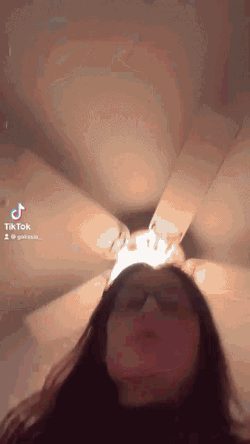 a woman wearing glasses is standing in front of a ceiling fan