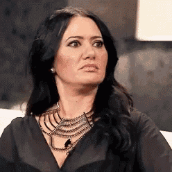 a woman wearing a black shirt and a necklace is looking at the camera .
