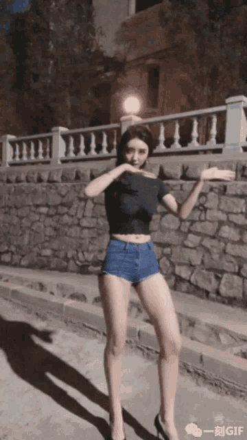 a woman wearing shorts and a black top is standing in front of a stone wall
