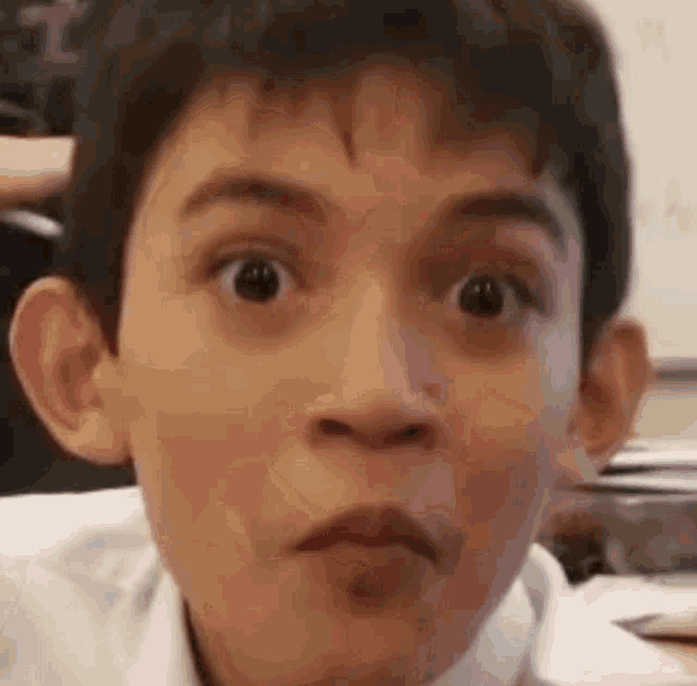 a young boy is making a funny face while sitting at a desk .