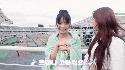 a girl wrapped in a green blanket stands next to another girl with red hair