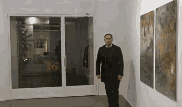 a man in a black coat stands in front of a door that says ' i 'm proud ' on it