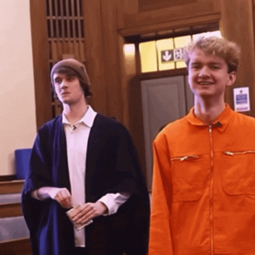 a man in an orange jacket stands next to another man in a black robe