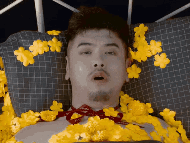 a man is laying on a bed with yellow flowers and a ribbon around his neck that says " for you "