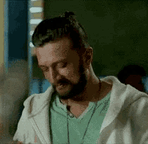 a man with a beard wearing a green shirt and a white hoodie is eating food .
