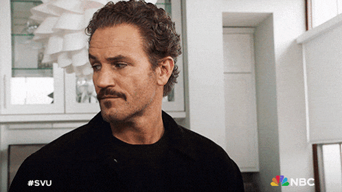 a man with a mustache is standing in a kitchen with a nbc logo behind him
