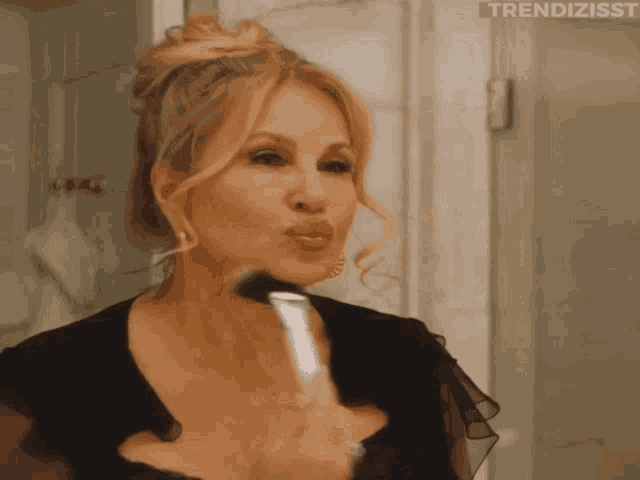 a woman in a black dress is applying makeup with a brush in front of a mirror with trendizisst written on the bottom