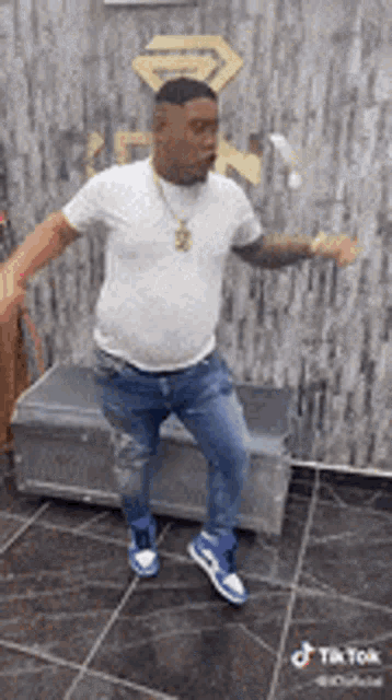 a man in a white shirt and blue jeans is dancing on a tiled floor in a room .