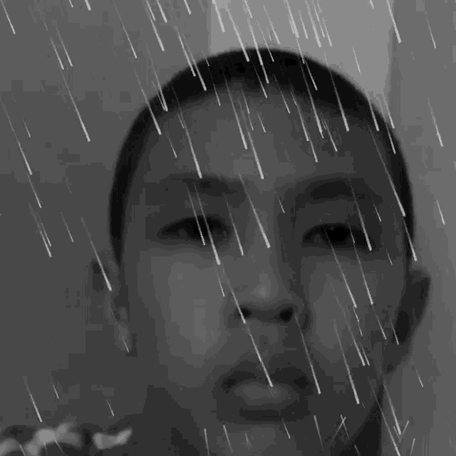 a black and white photo of a boy 's face with rain drops falling on it
