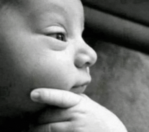 a black and white photo of a baby 's face with a hand on its chin .
