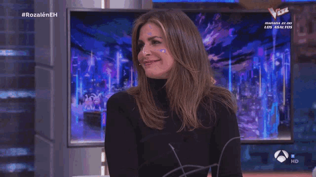 a woman applauds in front of a screen that says #rozaleneh on it
