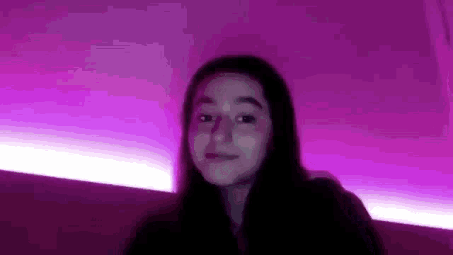 a young girl is sitting in front of a purple wall with a purple light behind her .