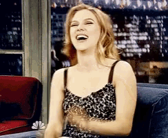 a woman is laughing while sitting on a couch in front of a window
