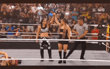 two female wrestlers are standing in a wrestling ring with a referee .