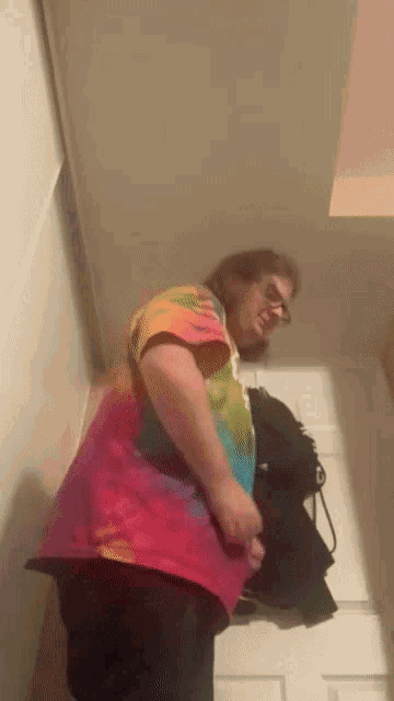 a man in a colorful tie dye shirt is standing in a hallway