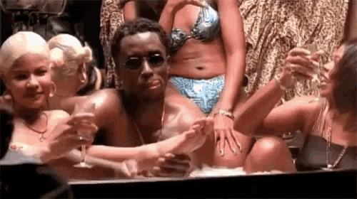 a man is sitting in a bathtub with a group of women holding wine glasses .