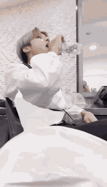 a man in a white shirt is drinking water from a plastic bottle .