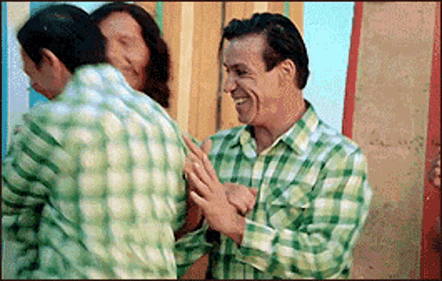 a man in a green and white plaid shirt is hugging another man