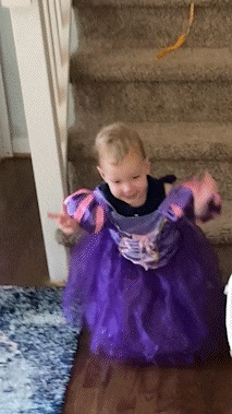 a little girl in a purple dress is sitting on the floor in front of a set of stairs