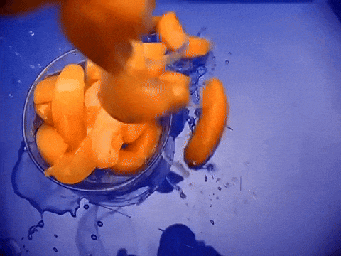 a bowl of sliced peaches is being poured into a blue bowl of water