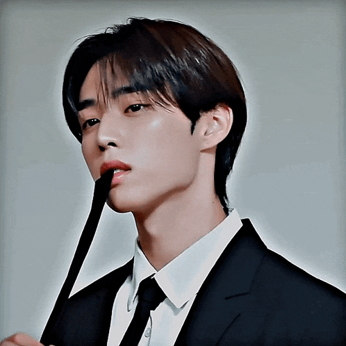 a young man in a suit and tie is holding a black stick in his mouth
