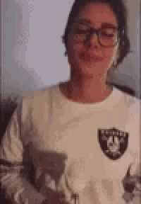 a woman wearing glasses and a raiders sweatshirt is holding a glass of wine .