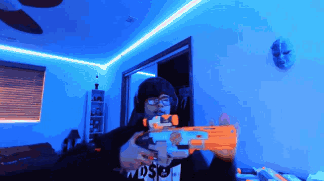 a person holding a nerf gun in a room with a mask on the wall