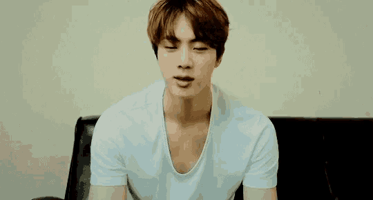a man in a white t-shirt is sitting on a couch .