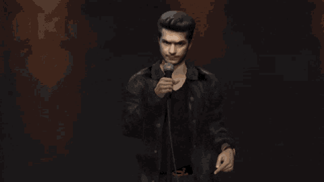 a man in a black jacket holds a microphone in his right hand