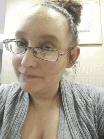 a woman wearing glasses and a gray sweater looks down