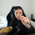 a woman is eating noodles with a spoon while sitting in a chair .