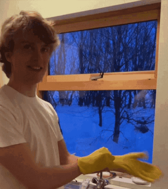 a young man wearing yellow rubber gloves is standing in front of a window