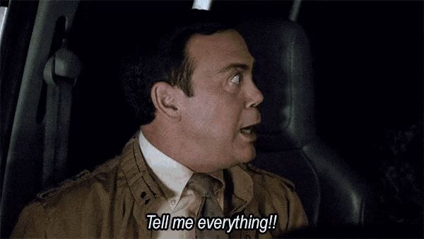 a man in a suit and tie is driving a car and yelling at the camera .