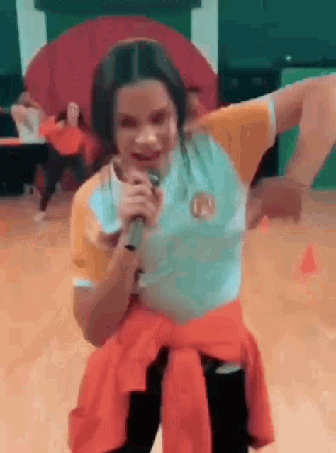 a young girl is singing into a microphone while dancing on a dance floor .