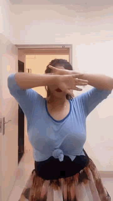 a woman in a blue shirt and a skirt is standing in front of a door .