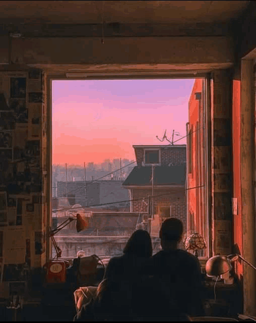 a man and a woman are sitting in a room looking out a window at a city .