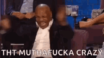 a man in a suit and tie is sitting in a chair with his legs crossed and laughing .