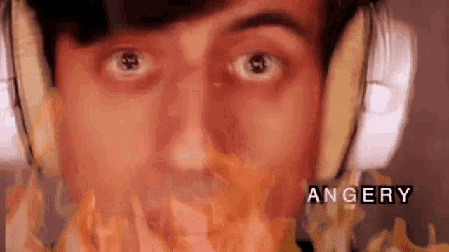 a close up of a man wearing headphones with a fire coming out of his mouth and the word angery in the corner .