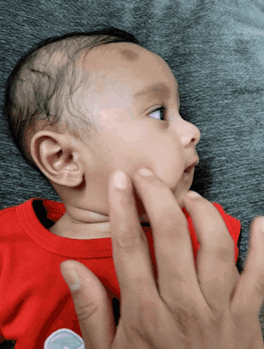 a baby in a red shirt is being touched by someone 's hand